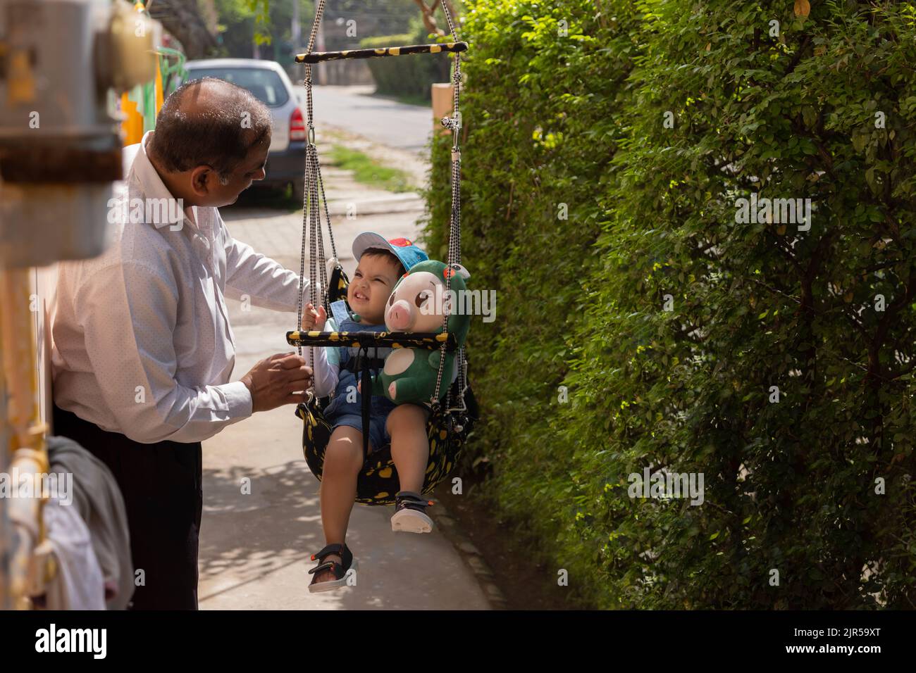 Großvater hat Spaß mit Enkelkind, das auf Schaukel sitzt Stockfoto
