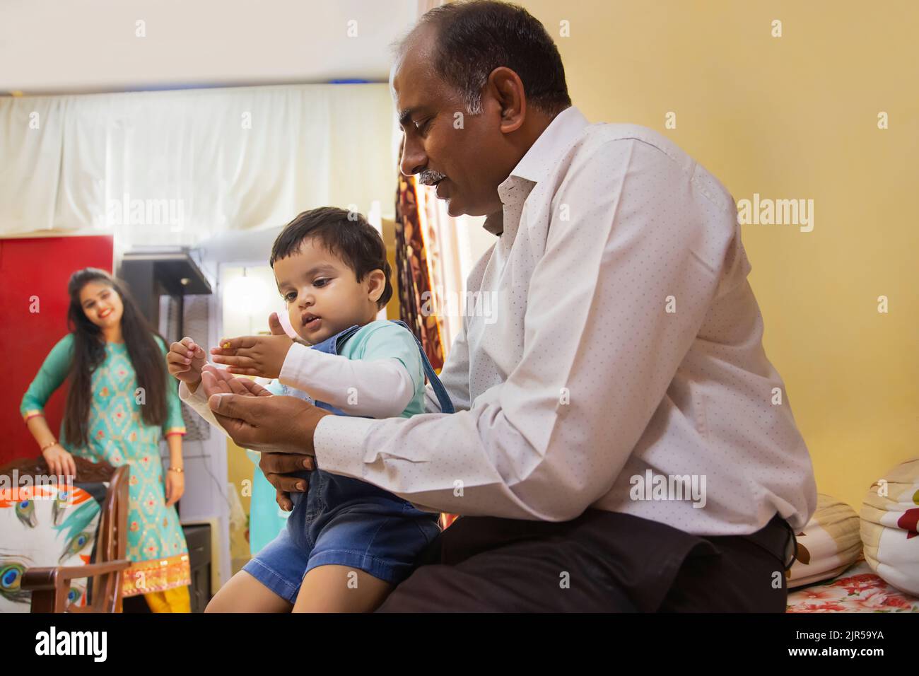 Enkel sitzt auf dem Schoß des Großvaters und Mutter steht weg Stockfoto