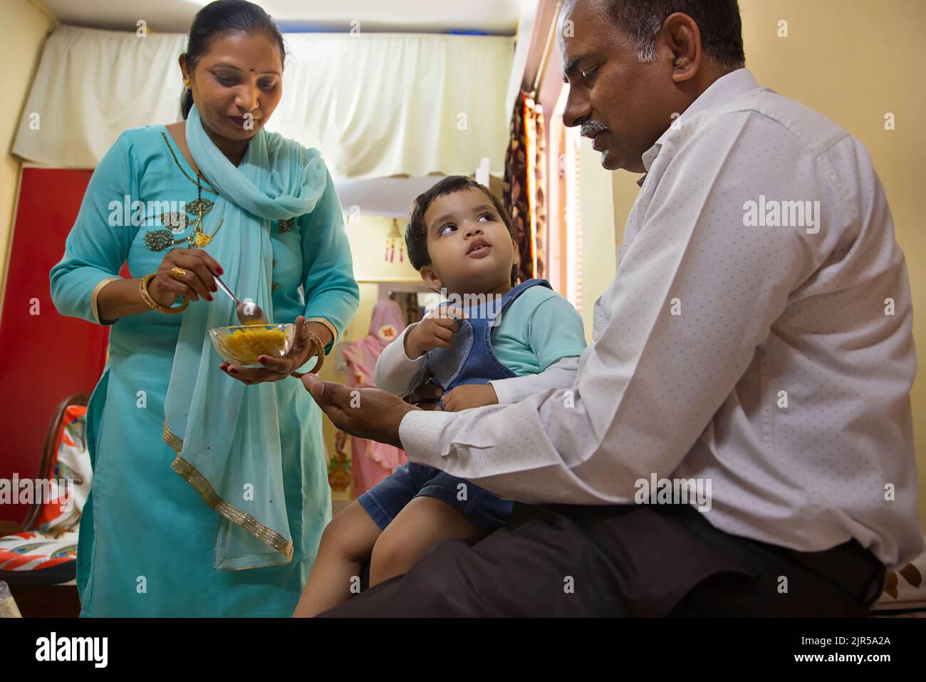 Großmutter füttert ihr Enkelkind, das auf dem Schoß des Großvaters sitzt Stockfoto