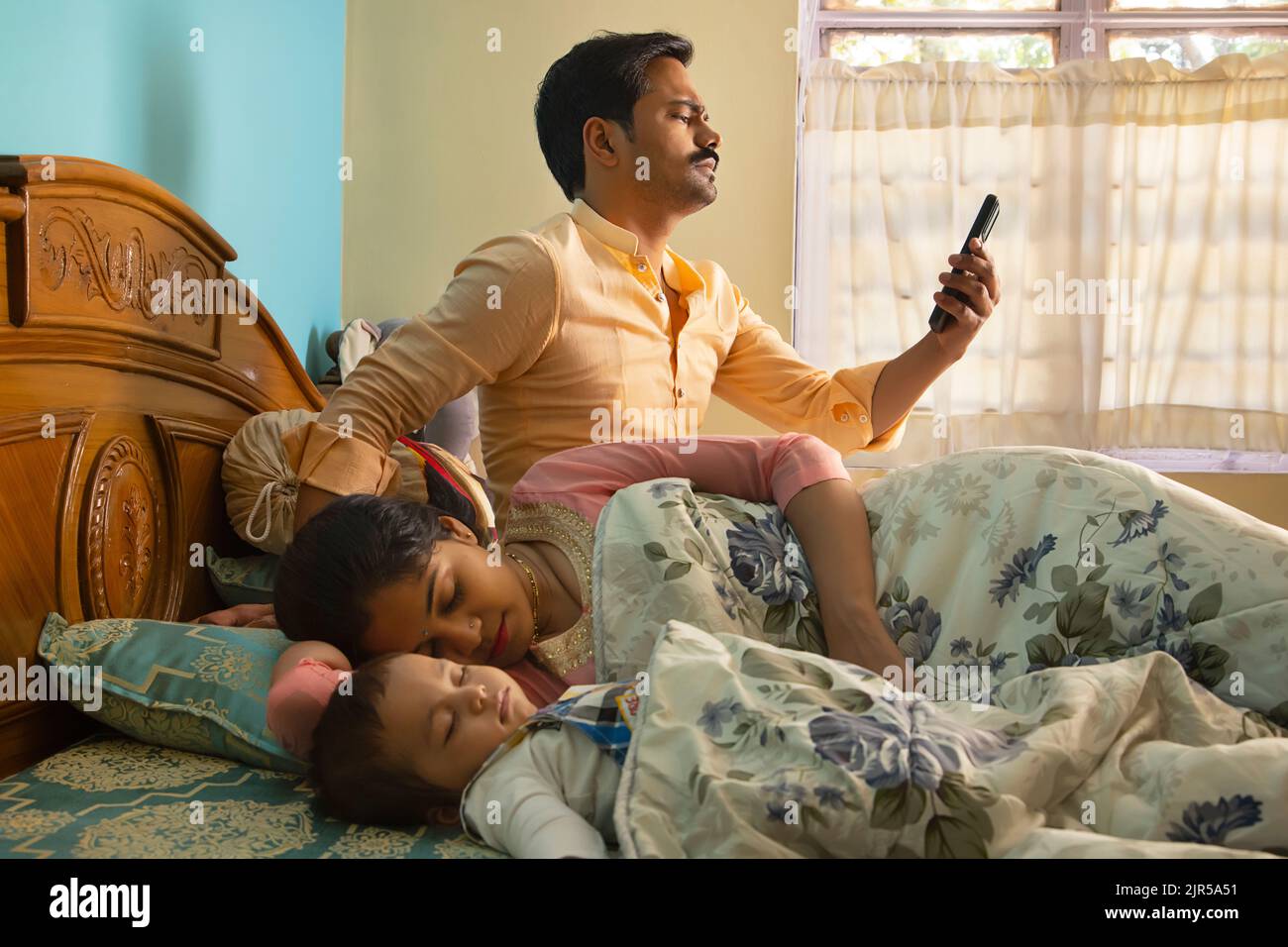 Vater benutzt Smartphone, während Mutter und Baby morgens im Bett schlafen Stockfoto