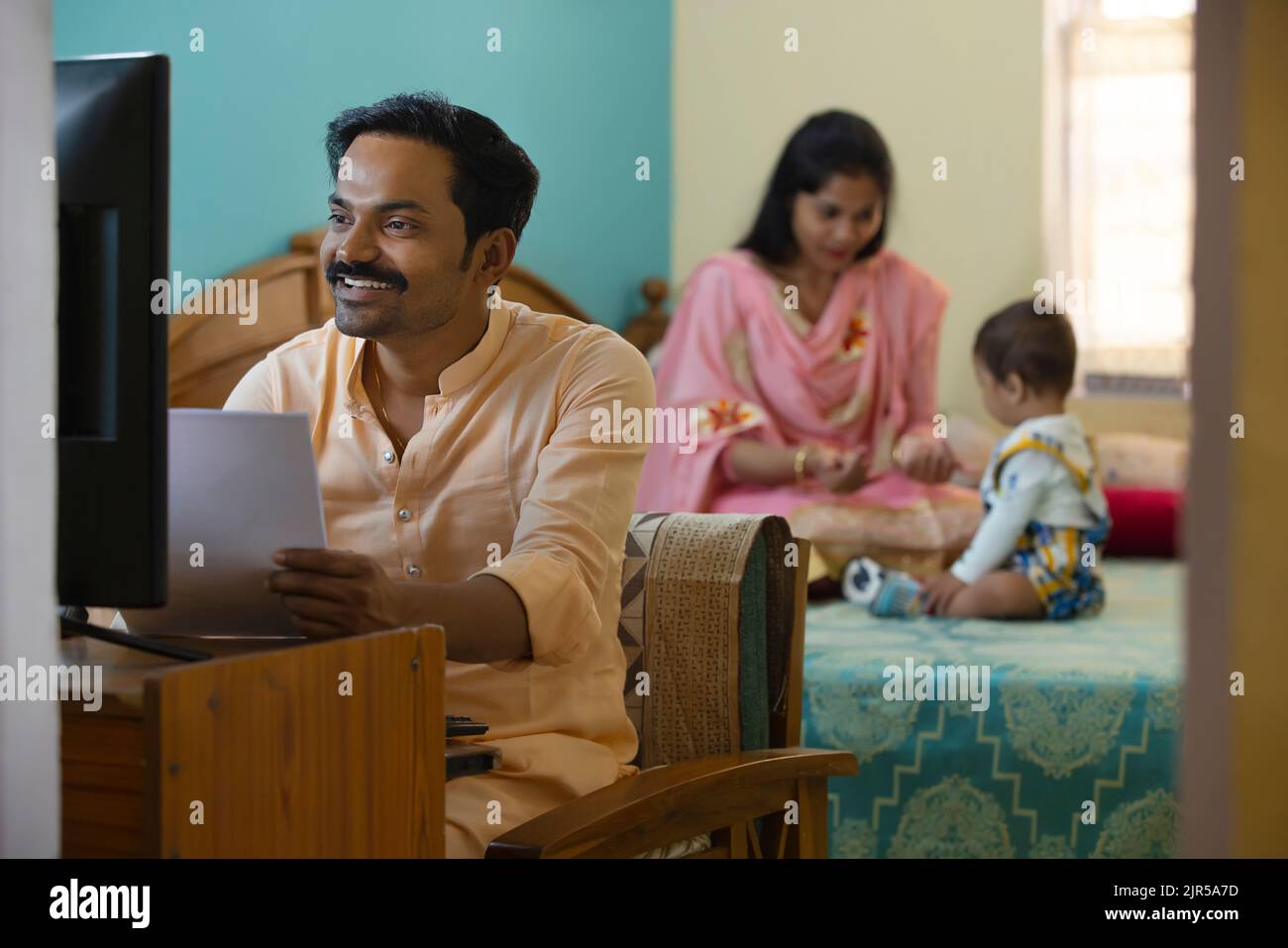 Vater arbeitet zu Hause, während Mutter mit ihrem Baby auf dem Bett spielt Stockfoto