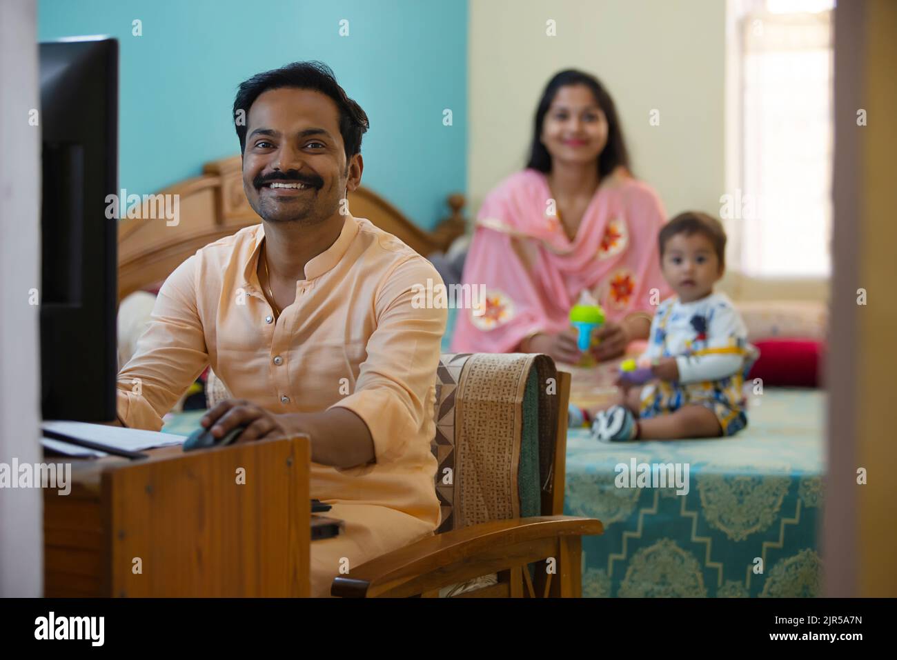 Vater arbeitet zu Hause, während Mutter mit ihrem Baby auf dem Bett spielt Stockfoto