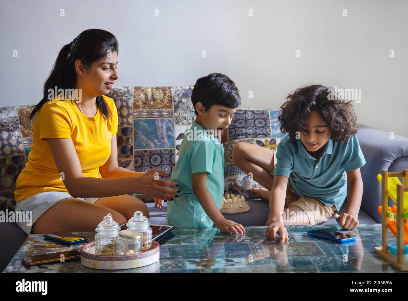 Kinder spielen zusammen und Mutter sitzt daneben im Wohnzimmer Stockfoto