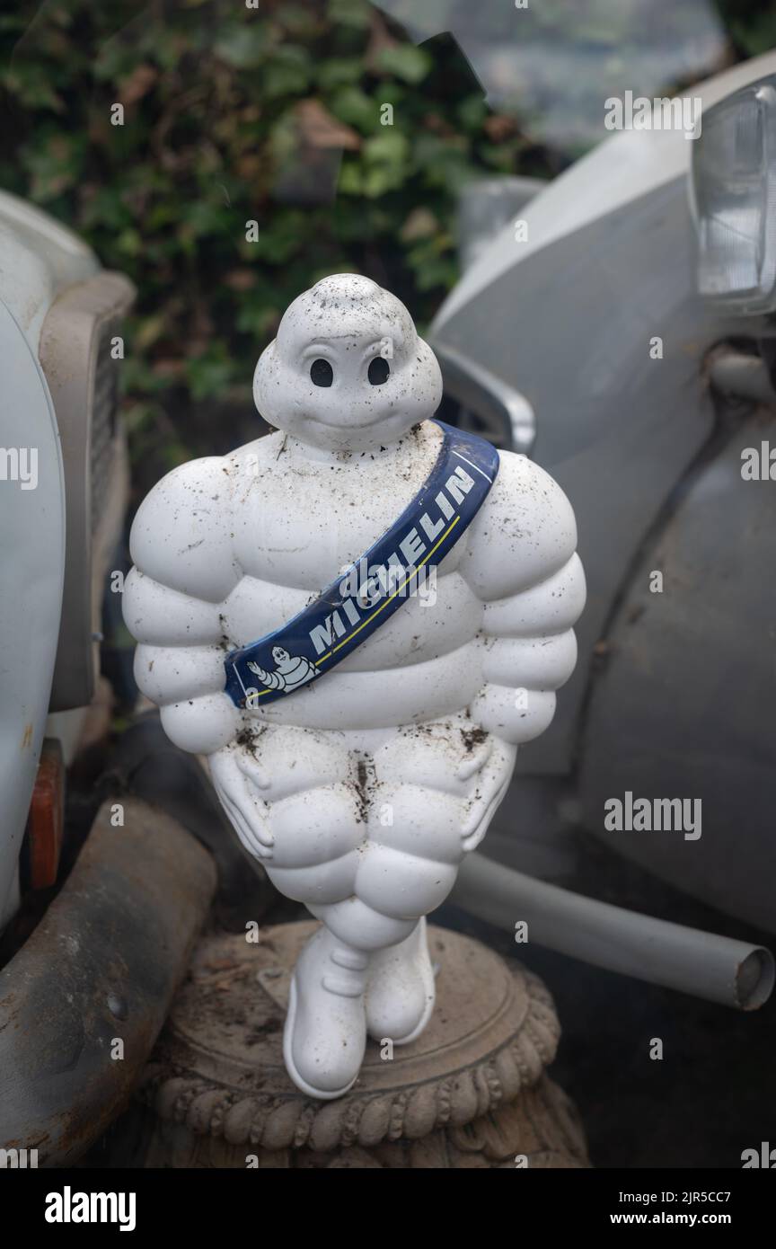 Eine vertikale Aufnahme der alten Michelin-Reifenpuppe zwischen zwei verlassenen Autos Stockfoto