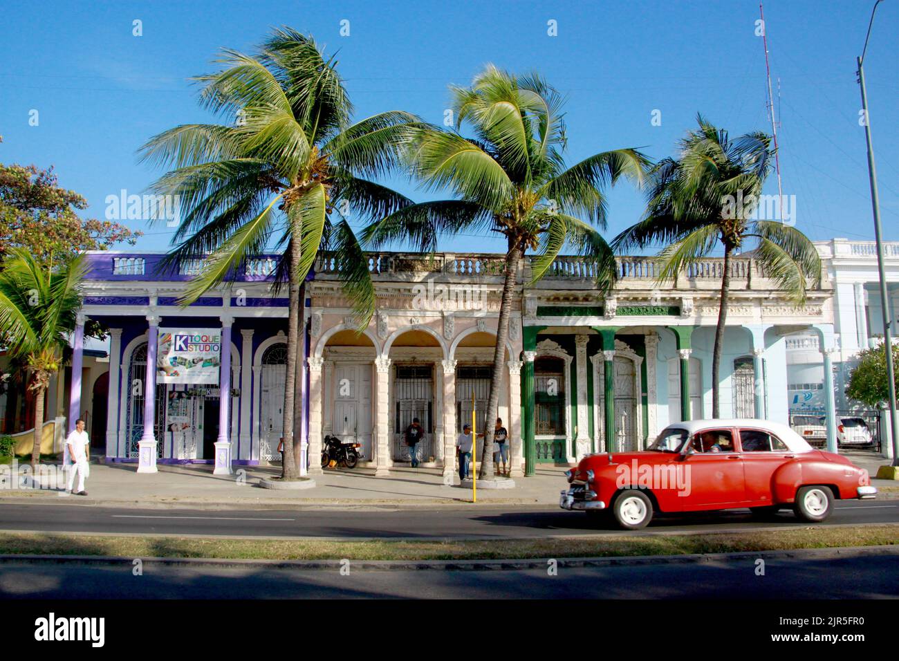 Ein altes rotes Auto am Straßenrand vor einem Gebäude mit Palmen in Malecon de Cienfuegos Stockfoto