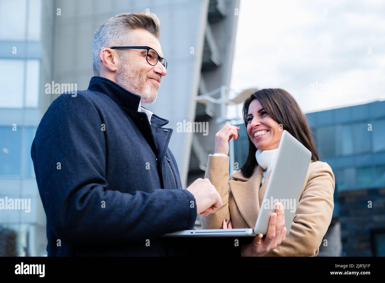 Geschäftsleute, die lächeln und neue Geschäftsideen zum Leben erwecken – zwei Mitarbeiter stehen und diskutieren über die Arbeit außerhalb des Büros Stockfoto