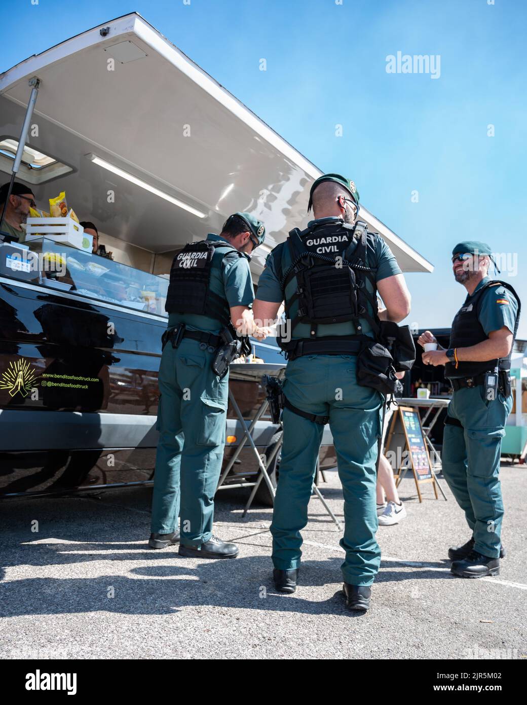 Eine vertikale Aufnahme der spanischen Guardia Civil, die an einem sonnigen Tag von einem Foodtruck isst Stockfoto