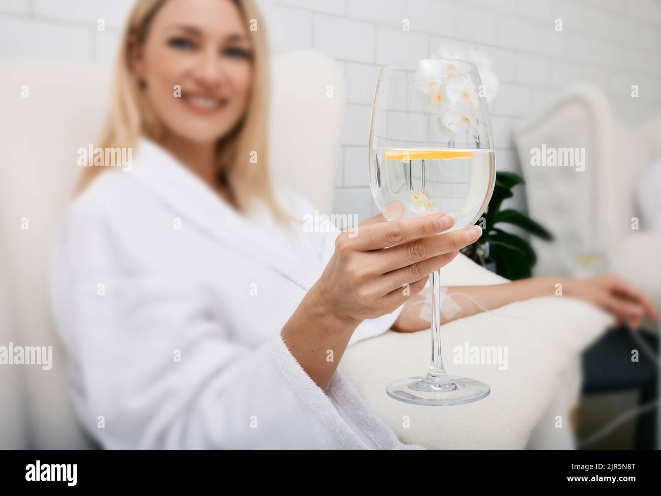Schöne Frau mit einem Glas erfrischenden Limettendrink während der intravenösen Entgiftungstherapie mit Infusion per Infusion. Entgiftungsbehandlungen im Spa Stockfoto