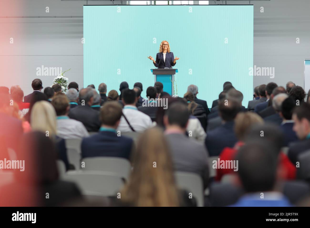 Eine Frau, die auf einem Podium eine Rede hält, und Personen, die auf einer Geschäftskonferenz im Publikum sitzen Stockfoto