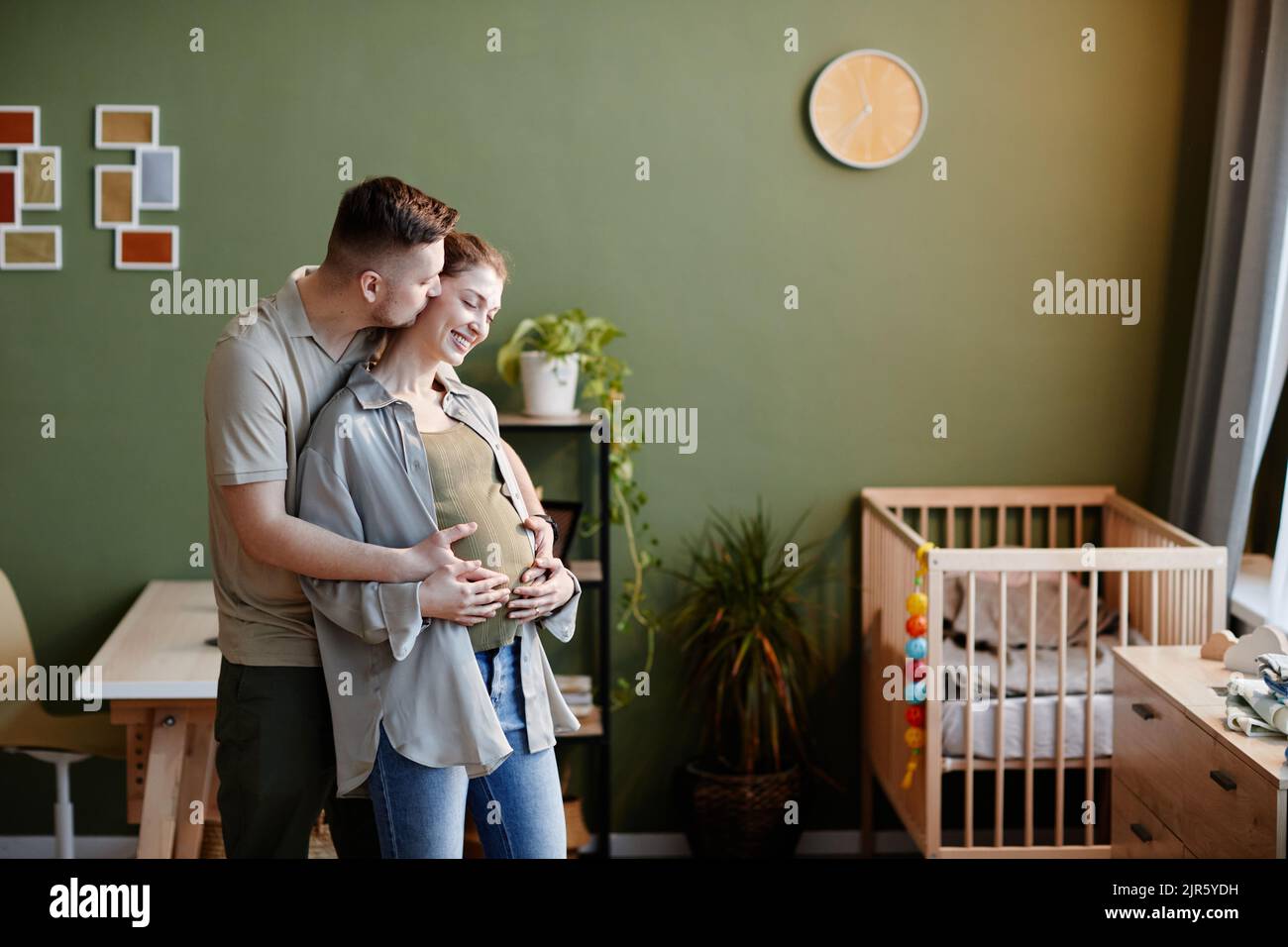 Junger Mann küsst sich und kümmert sich um seine Schwangere, während sie im Zimmer stehen Stockfoto