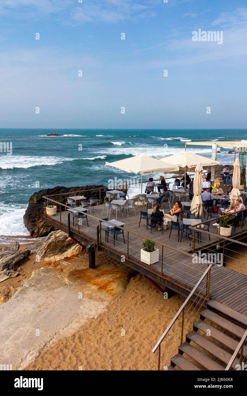 Wellen schlagen gegen Felsen an einem Strand in der Nähe eines Cafés und einer Bar an der Atlantikküste in Foz do Douro in der Nähe von Porto im Norden Portugals. Stockfoto