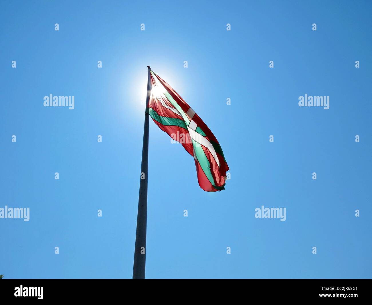 Die Ikurrina-Flagge winkt in der Luft gegen den blauen wolkenlosen Himmel und bedeckt die Sonnenstrahlen Stockfoto