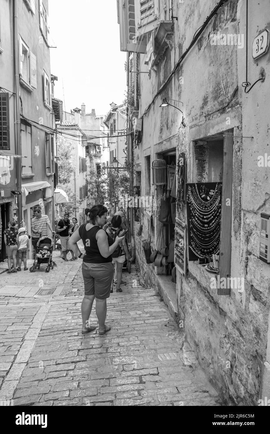 Eine vertikale und monochrome Aufnahme der Menschen, die in einer engen Straße im Zentrum von Rovinj, Kroatien, spazieren gehen Stockfoto