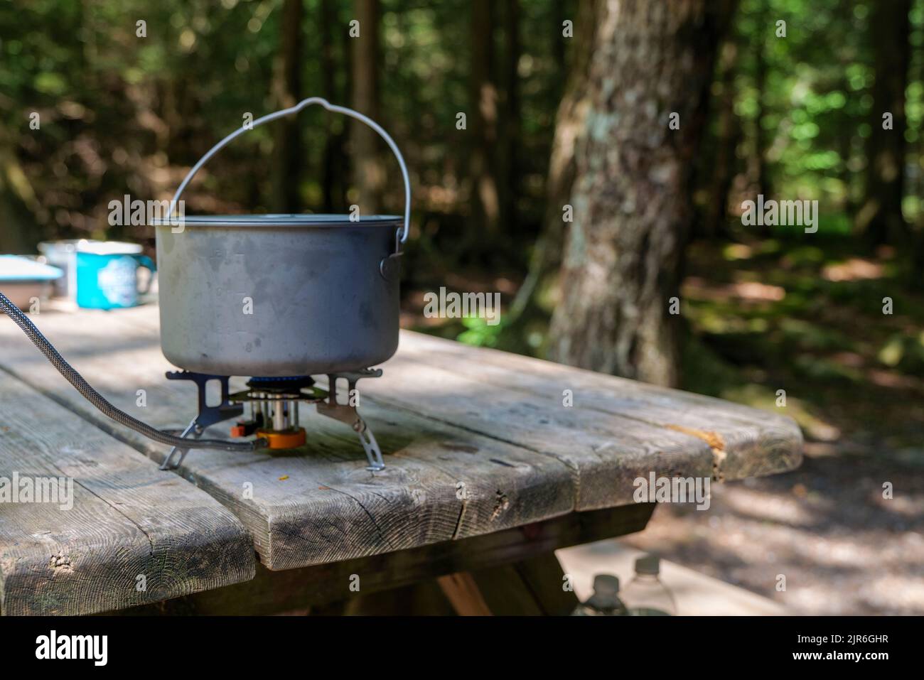 Ein Titantopf zur Herstellung von Lebensmitteln auf einem Gasherd auf einem Campingtisch aus Holz im Wald. Stockfoto