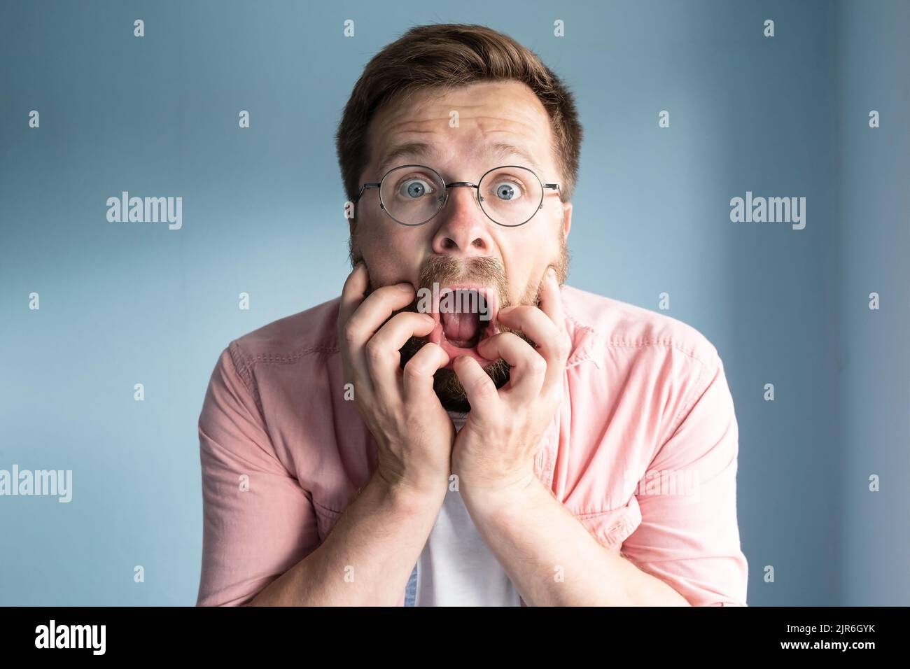 Der Mann mit Brille ist sehr verängstigt, er hält die Hände im Gesicht, er öffnet den Mund schockiert und sieht mit großen Augen. Stockfoto