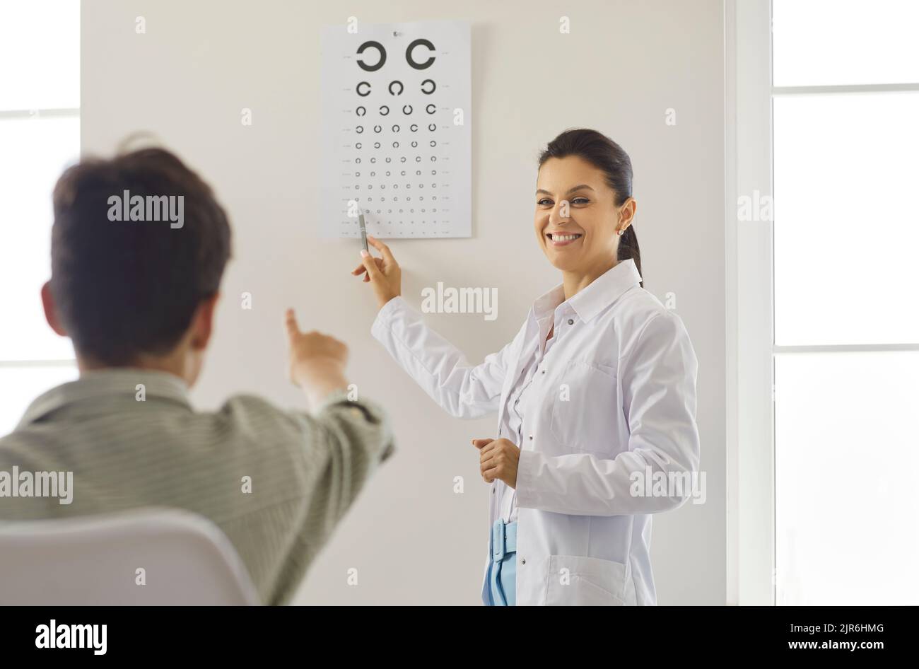 Ein freundlicher Optiker überprüft die Sehkraft des Jungen in der Augenklinik mit Hilfe der Testkarte. Stockfoto