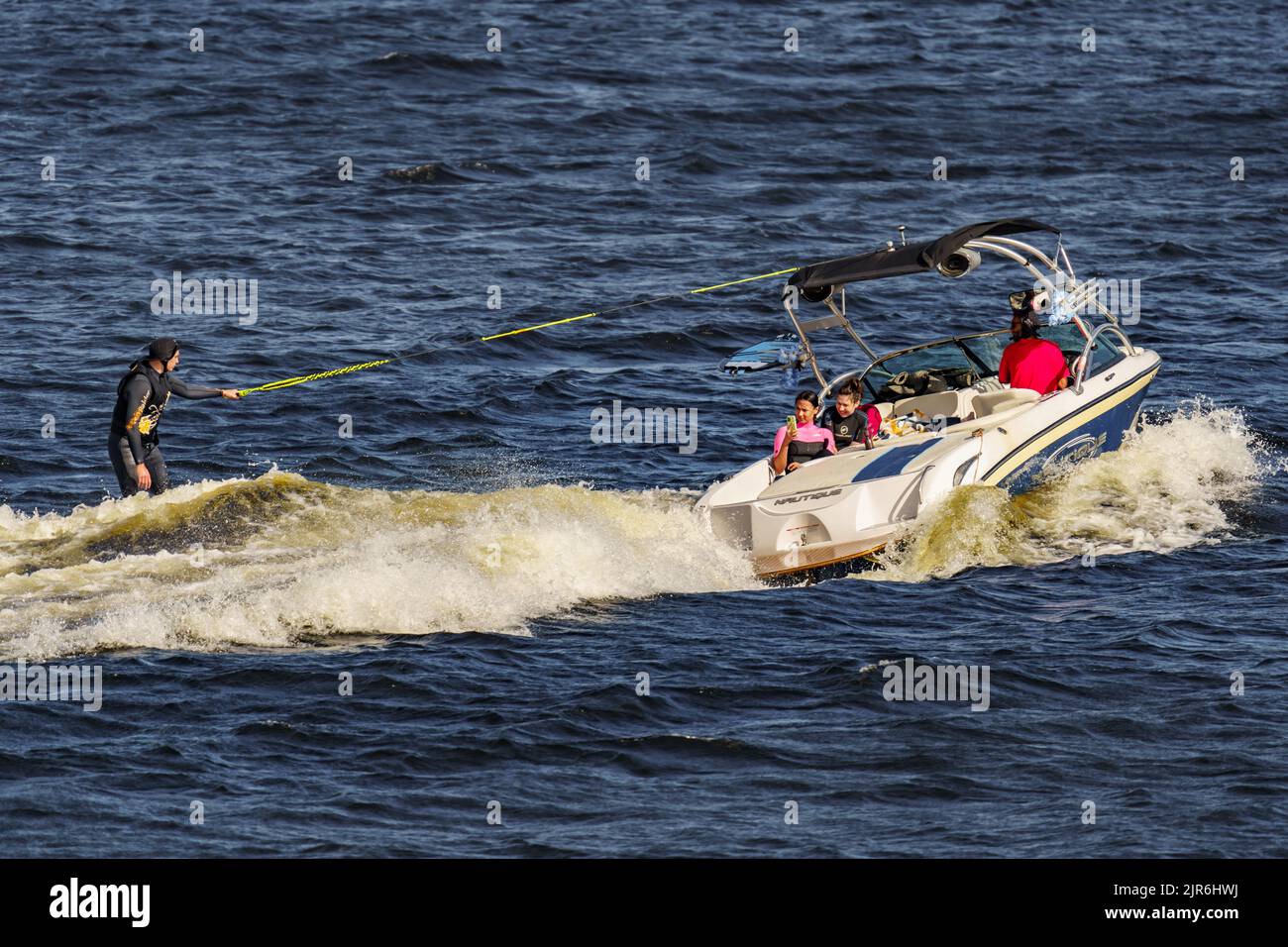 Russland, St. Petersburg, 29. Juli 2022: Mann auf Wakeboard auf Welle des Motorbootes im Sommerfluss, Wakesurfen auf Fluss Sommerferien Stockfoto
