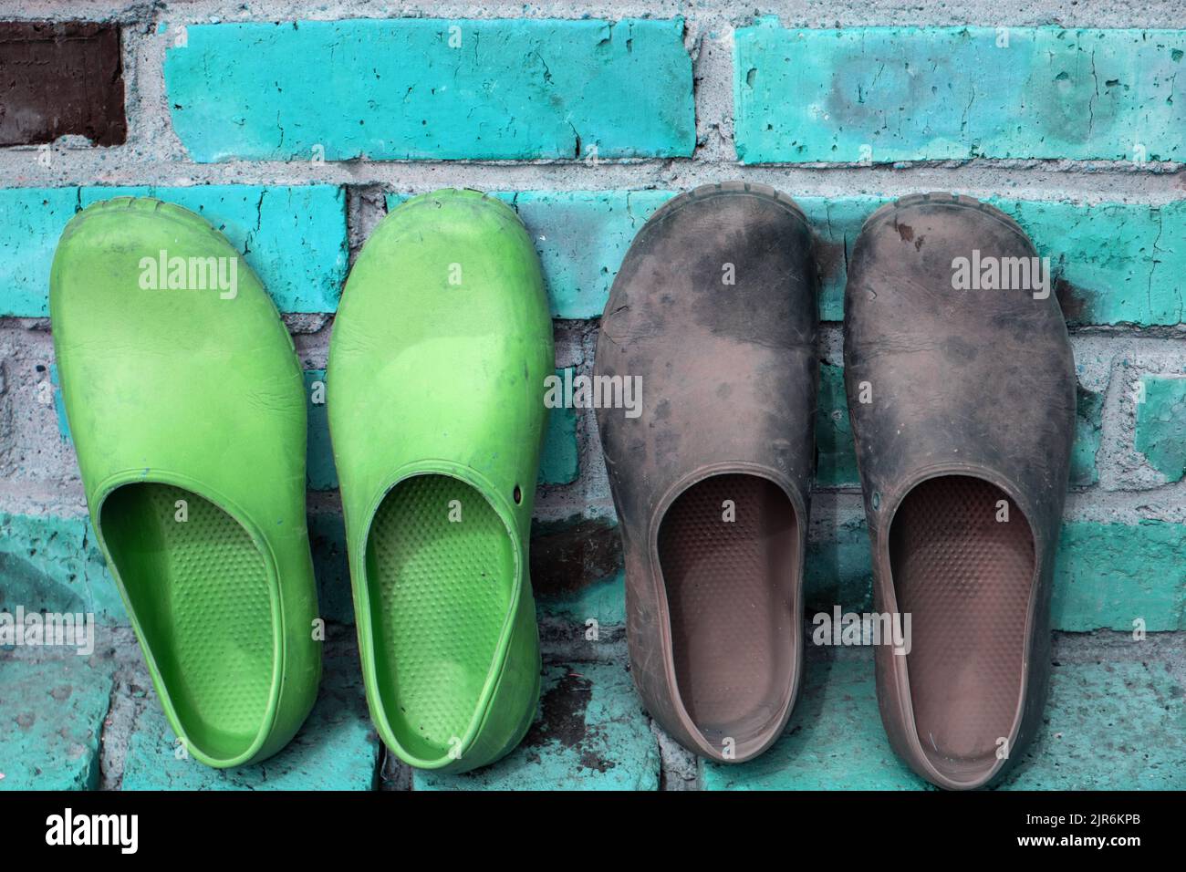 Zwei Paar schwarze und grüne Gummigaloshes gegen eine blaue Ziegelwand Stockfoto