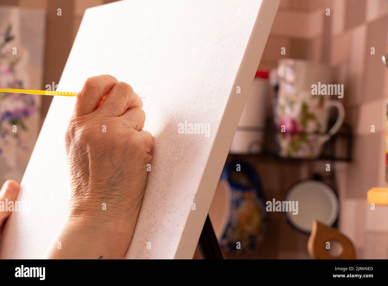 Alte weibliche Hände zeichnen ein Bild zu Hause mit einem Pinsel auf eine Leinwand, zeichnen ein Bild und ein Hobby, eine Künstlerin Stockfoto