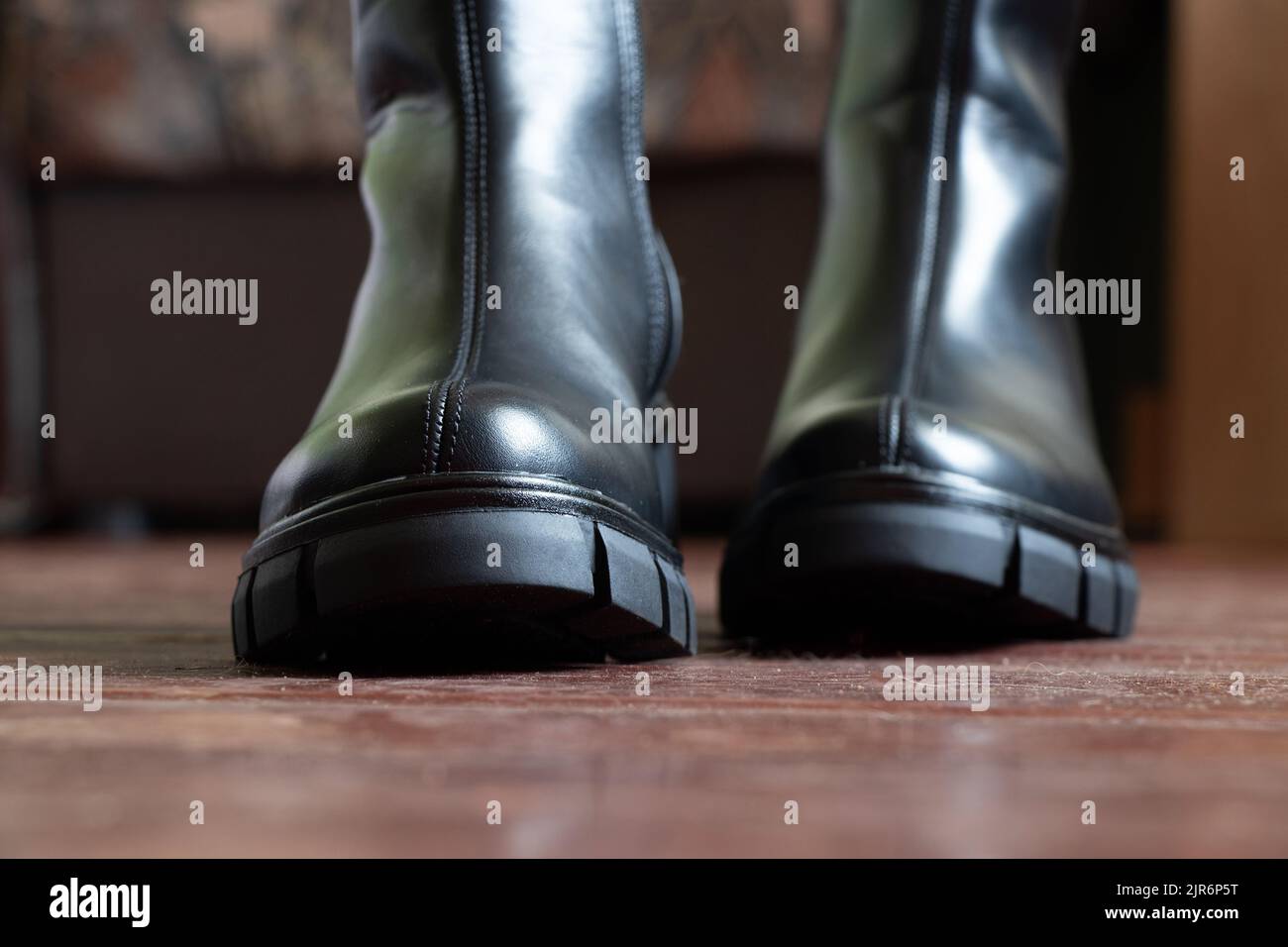 Mädchen in hohen schwarzen Stiefeln auf dem alten schmutzigen Boden zu Hause, Damenschuhe, Füße in Schuhen auf dem Boden, Schuhe auf dem Holzboden Stockfoto