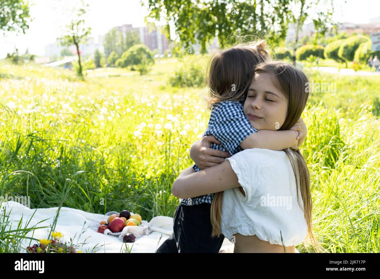 Bruder und Schwester spielen im Park inmitten des grünen Grases. Kinder umarmen sich fest. Picknick außerhalb der Stadt. Kindheit. Beziehungen. Stockfoto