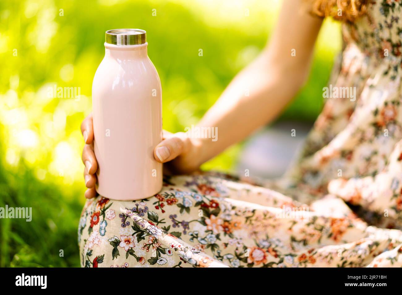 Nahaufnahme der Stahl Eco Thermo Wasserflasche in weiblicher Hand. Grüner Hintergrund im Park. Konzept für den Kopierraum. Platz für Text. Kunststoff frei. Zero Waste Konzept. Selektiver Fokus. Stockfoto