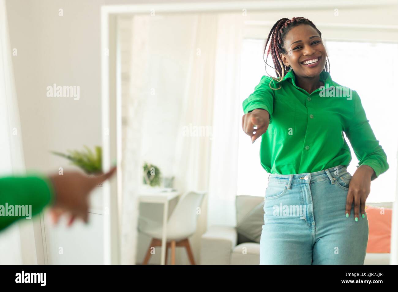 Wellness-Konzept. Fröhliche schwarze Dame, die neben dem Spiegel tanzt und ihr Spiegelbild anlächelt und Spaß im Schlafzimmer hat Stockfoto