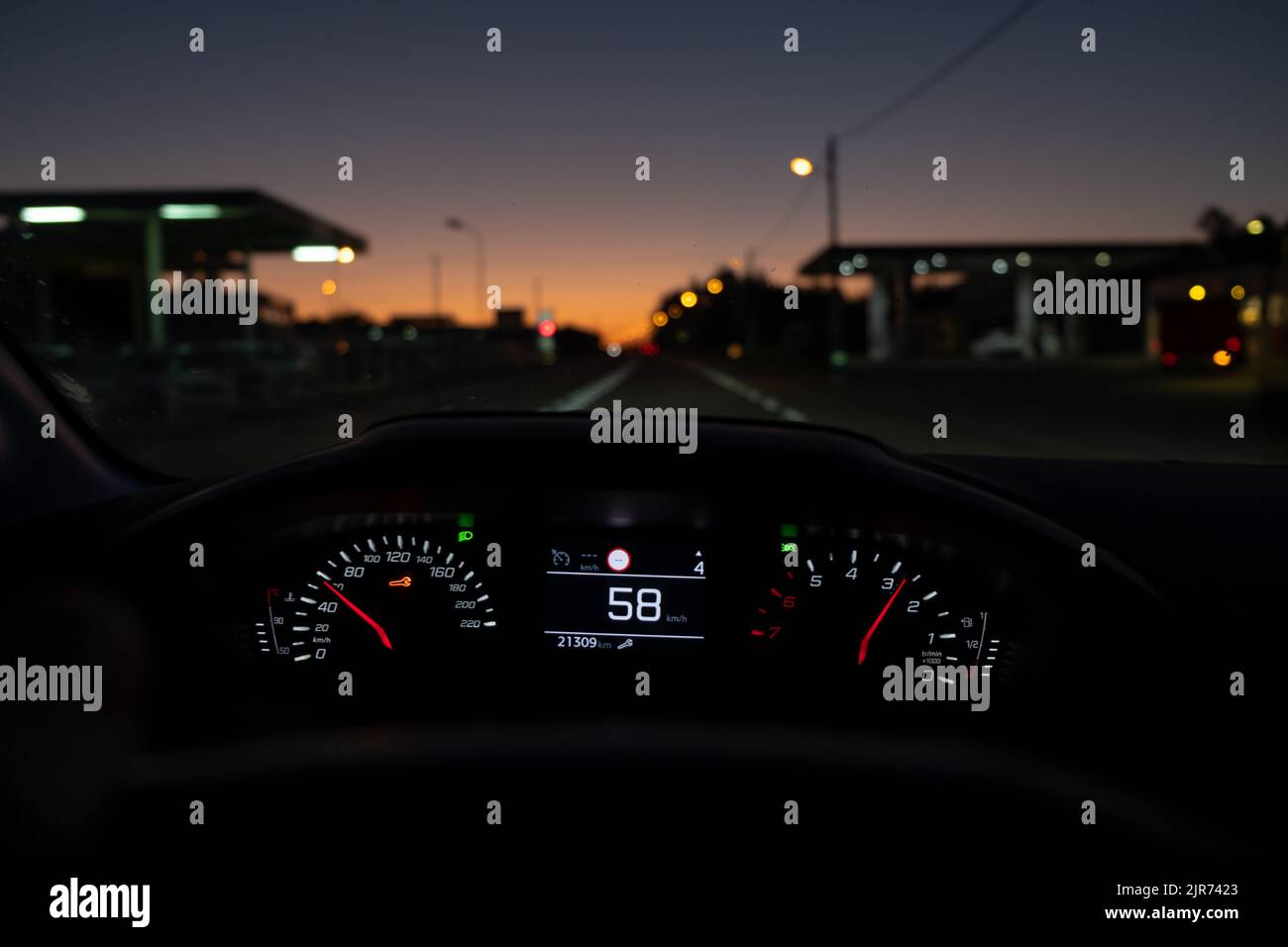 Blick des Fahrers auf den Tachometer bei 58 km/h oder 58 mph, auf einer Straße mit Lichtern und Bahnhofsdiensten auf beiden Seiten, die in Bewegung verwackelt sind, im nächtlichen Fall POV. Stockfoto