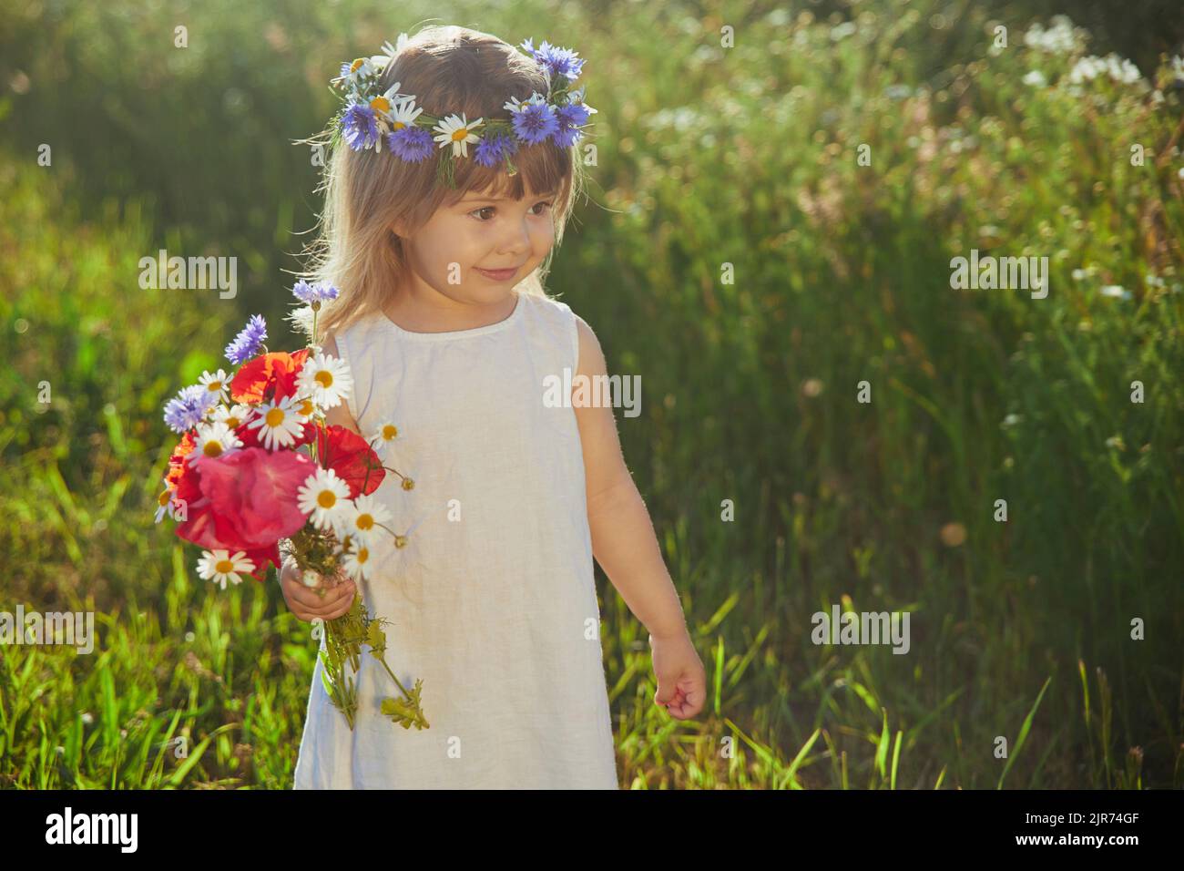 Charmantes Kind in Leinenkleid geht in einem Feld mit Blumen Stockfoto