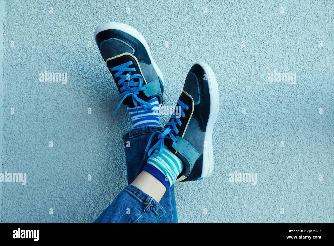 Kind trägt verschiedene Socken. Kinderbeine in nicht passenden Socken auf grauem Hintergrund. Tag der ungeraden Socken, Woche der Anti-Mobbing-Bekämpfung. Down-Syndrom-Bewusstsein Stockfoto