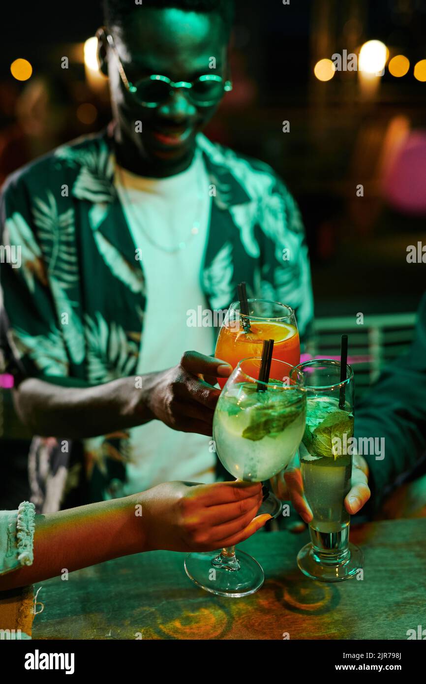 Eine Gruppe junger Freunde, die sich an der Theke versammelt hatten, klimmten mit Gläsern Cocktails, während sie auf der Dachterrasse eine Party oder im Nachtclub Spaß hatten Stockfoto