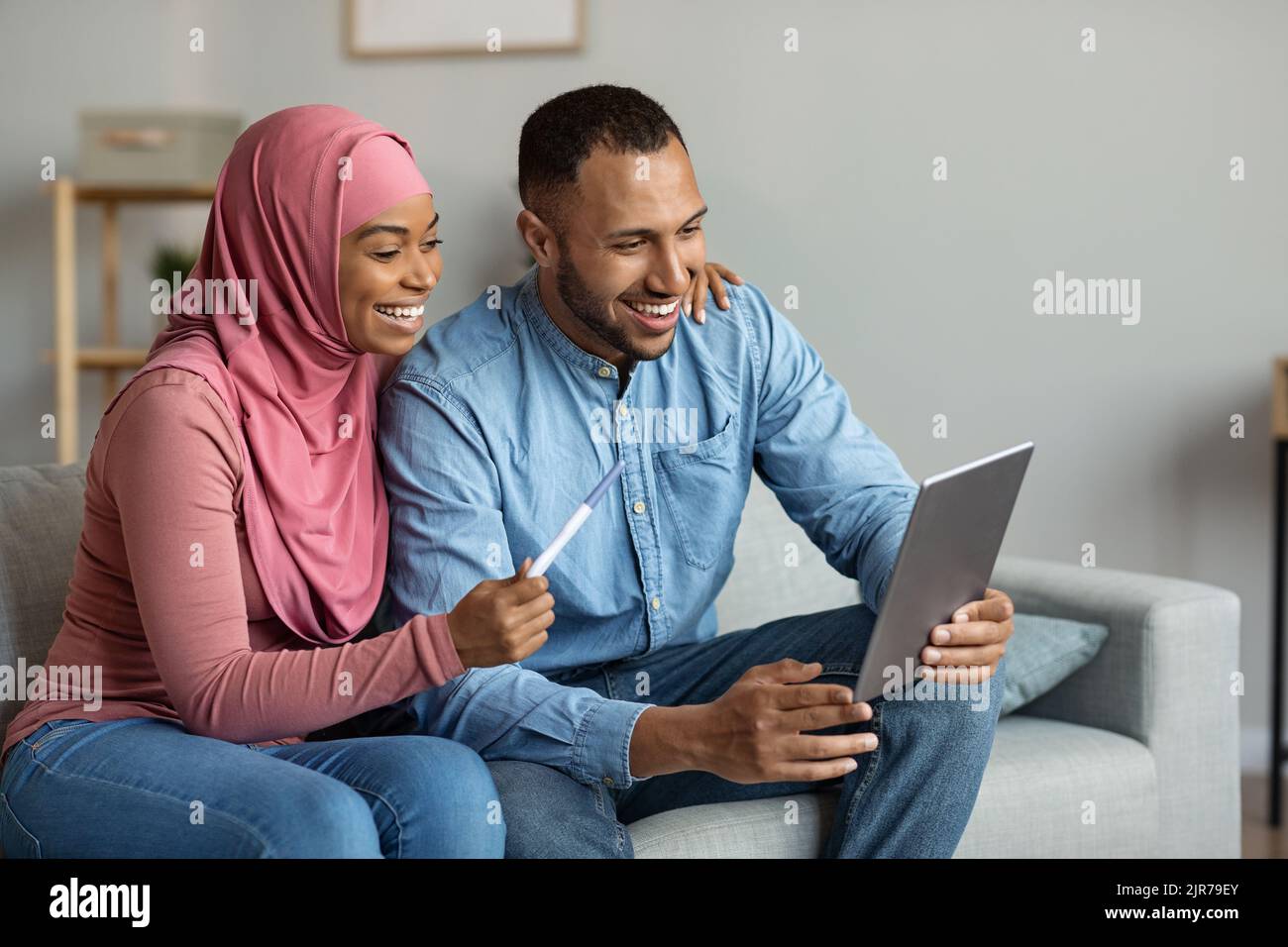 Fröhliche Muslimische Ehegatten, Die Mit Einem Digitalen Tablet Einen Videoanruf Tätigen Und Schwangerschaftsnachrichten Teilen Stockfoto