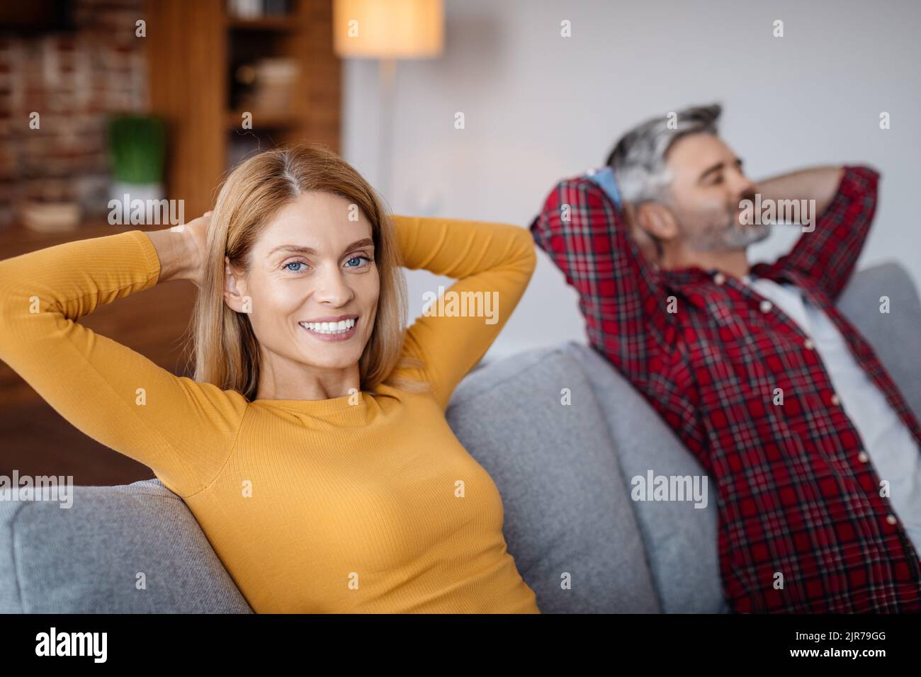 Fröhliche, ruhige, reife kaukasische Männer und Frauen, die sich auf dem Sofa entspannen, in die Kamera schauen, Freizeit im Wohnzimmer genießen Stockfoto