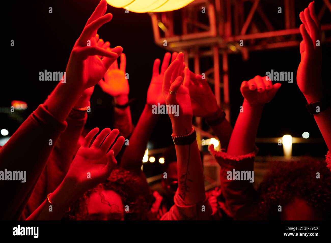 Hochgezogene Hände junger, energischer Freunde, die nachts auf der Dachparty im Café im Freien tanzen und ihre Zusammenkünfte genießen Stockfoto