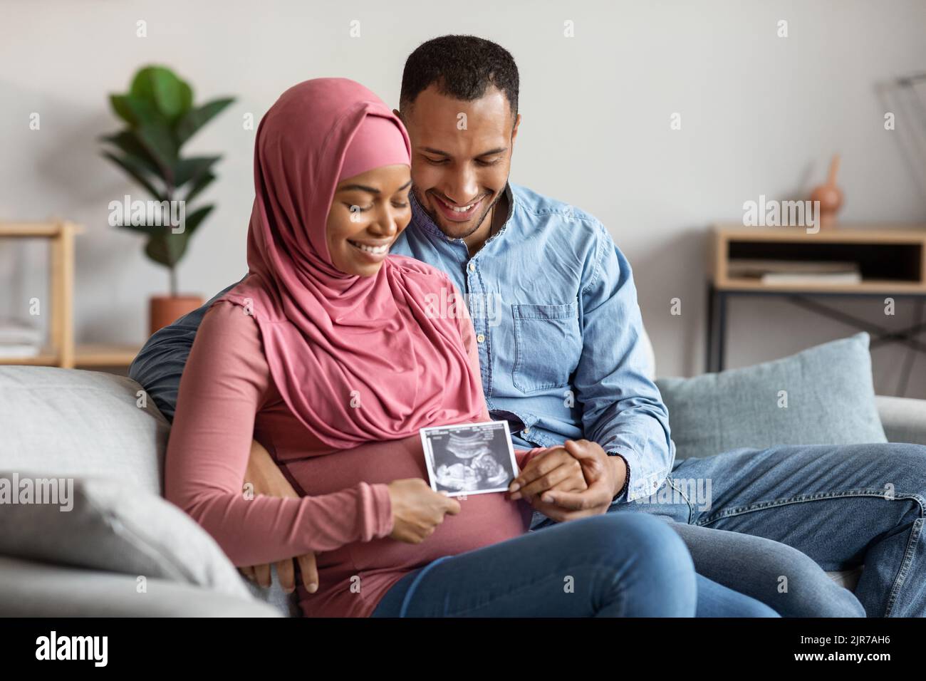 Schwarzes Schwanger Islamisches Paar Hält Baby Ultraschall-Scan, Während Sie Auf Der Couch Sitzt Stockfoto