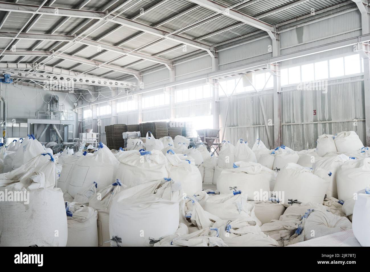 Teil eines geräumigen Lagerhauses oder Lagerraums mit Haufen riesiger weißer Säcke, die lose Rohstoffe für die industrielle Produktion enthalten Stockfoto