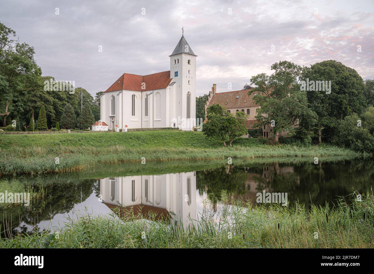 Eine ländliche Szene mit einer weißen skandinavischen Kirche, die sich im spiegelartigen See beim Sonnenuntergang widerspiegelt, Mariager, 7. August 2022 Stockfoto