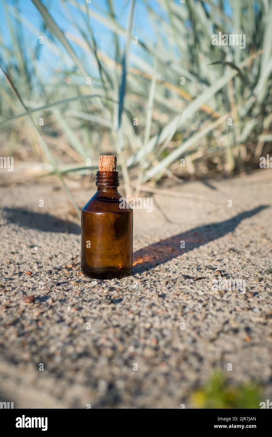 Flasche ätherisches Öl an einem Sandstrand. Kleine braune Medizinflasche im Hintergrund der Natur. Hanföl aus biologischem CBD. Stockfoto