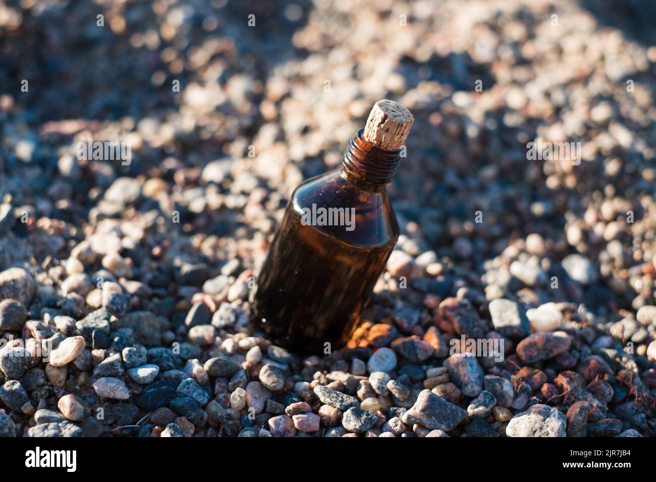 Flasche ätherisches Öl an einem Sandstrand mit Felsen. Kleine braune Medizinflasche im Hintergrund der Natur. Hanföl aus biologischem CBD. Stockfoto