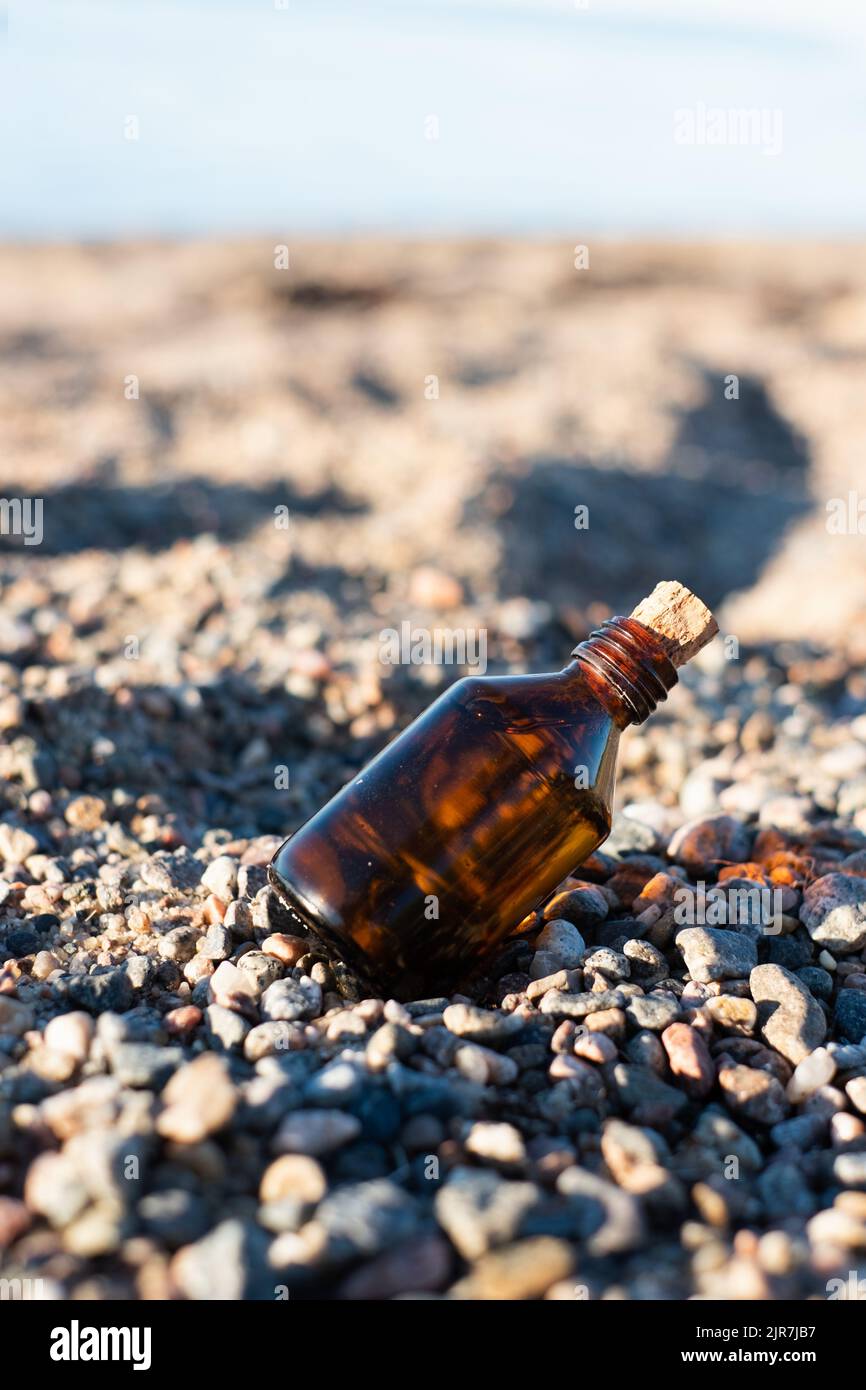 Flasche ätherisches Öl an einem Sandstrand mit Felsen. Kleine braune Medizinflasche im Hintergrund der Natur. Hanföl aus biologischem CBD. Stockfoto