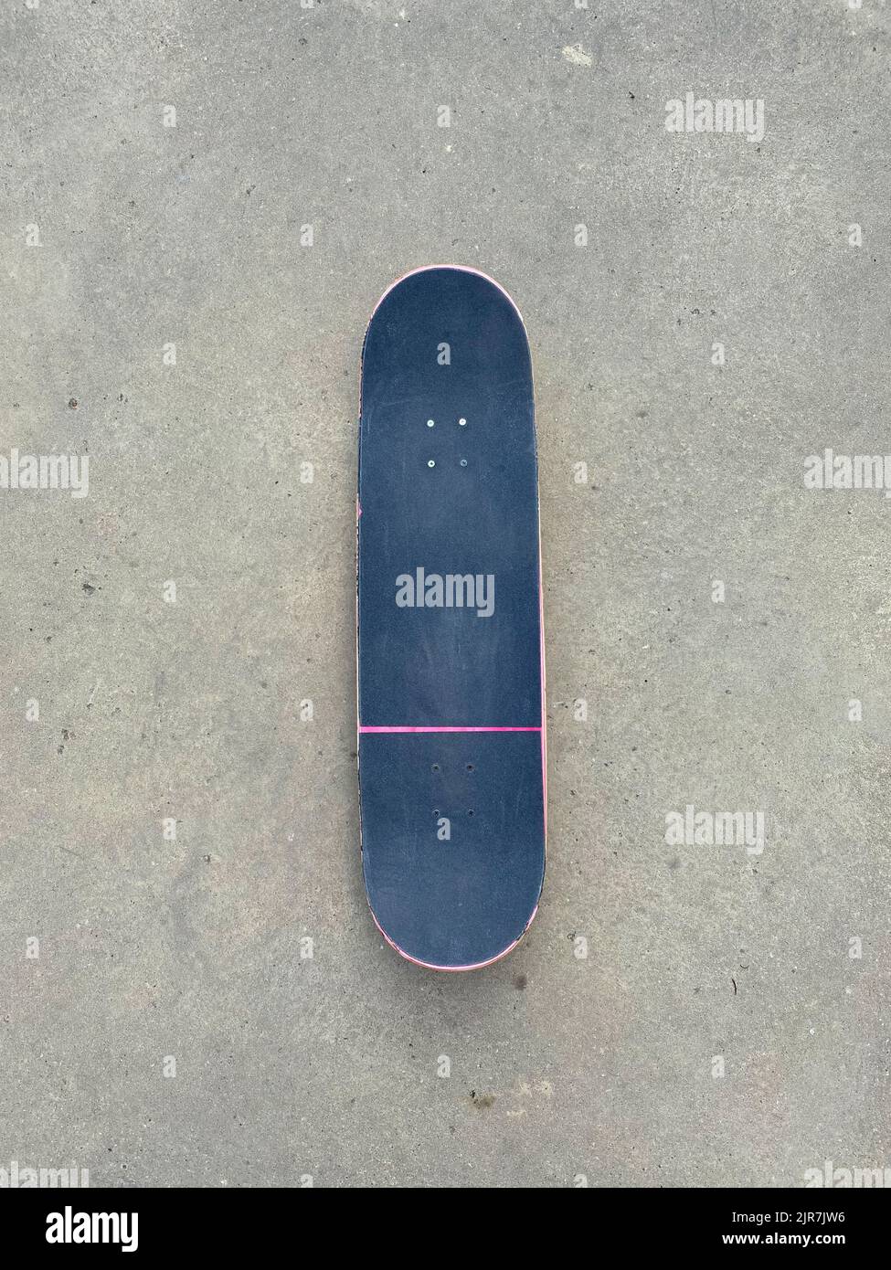 Rosafarbenes Skateboard, das auf einer glatten Betonoberfläche im lokalen Skatepark liegt - schwarzes Griptape Stockfoto