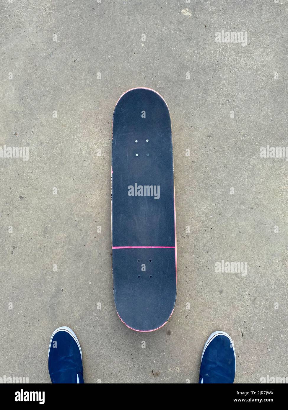 Rosafarbenes Skateboard, das auf einer glatten Betonoberfläche im lokalen Skatepark liegt - schwarzes Griptape Stockfoto