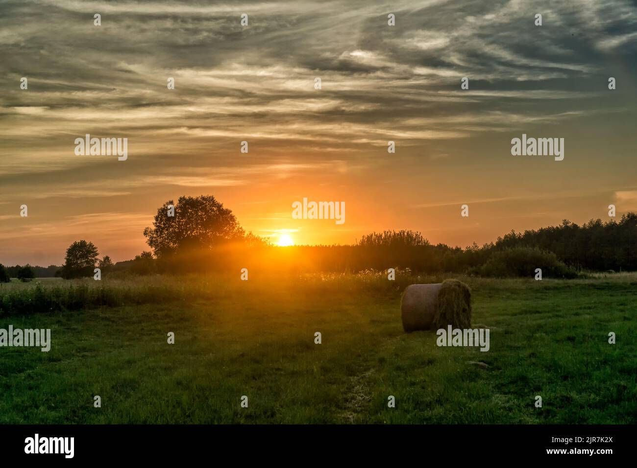 Sonnenuntergang über der Wiese mit Heuballen im Sommer. Landschaft des Nationalparks Biebrza in Polen, Europa. Dramatische Wolken über dem Grasland. Stockfoto
