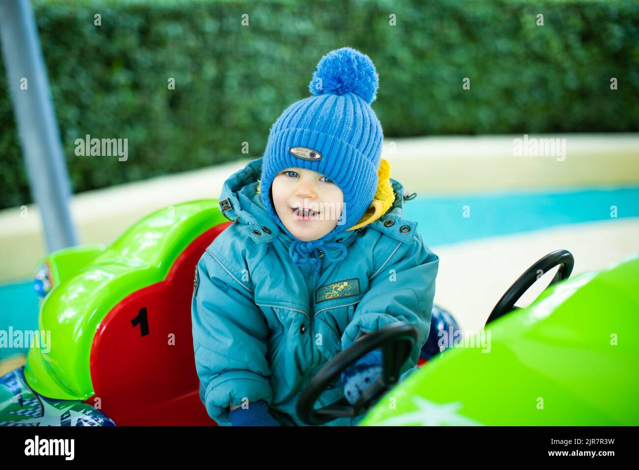 Fröhlicher kleiner Junge, der ein Auto auf einer fröhlichen Runde fährt Stockfoto