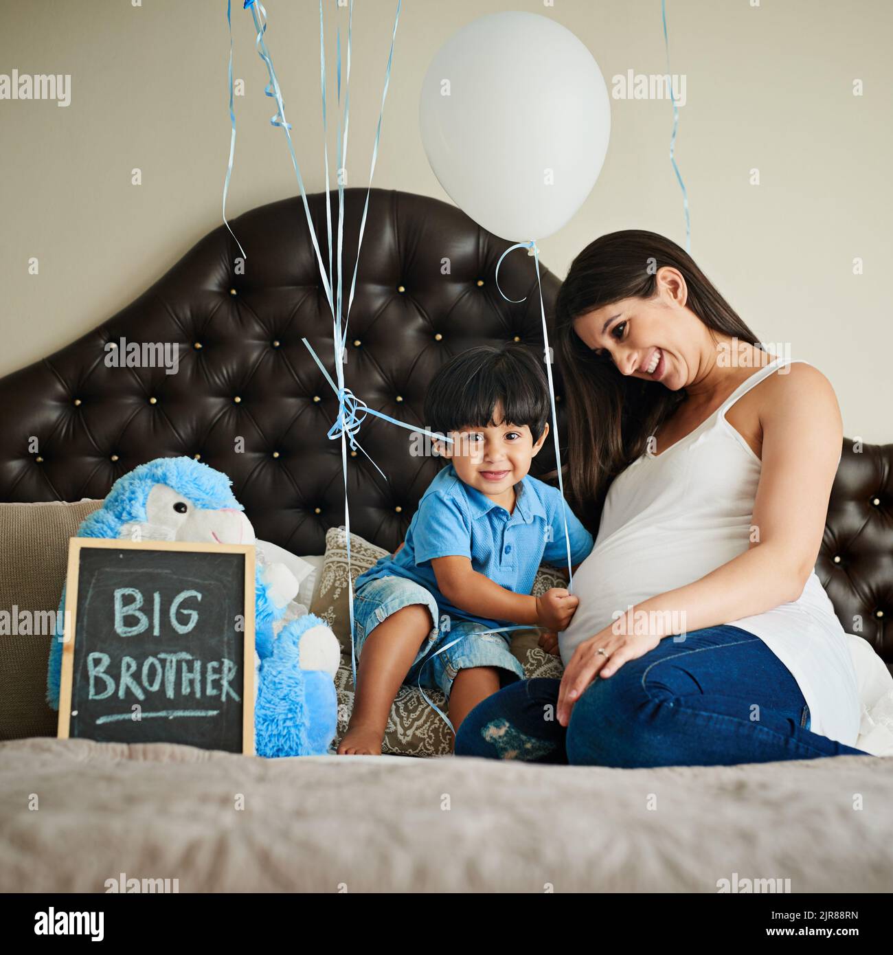 Mummys hat eine Überraschung für Sie. Eine glückliche Schwangere, die sich mit ihrem kleinen Jungen zu Hause auf ihrem Bett festklebte. Stockfoto