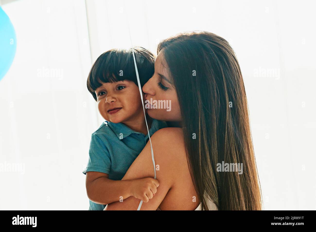 Zeit zum Kuscheln mit Mama. Eine junge Mutter kuschelt ihren kleinen Jungen, während er einen Ballon zu Hause hält. Stockfoto