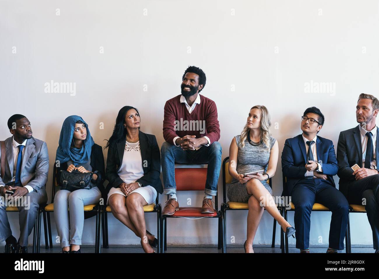 Seien Sie die Ausnahme, auf die sie gewartet haben. Eine Gruppe von selbstbewussten Geschäftsleuten wartet in der Schlange auf ihre Interviews, während ein Mann auf einem sitzt Stockfoto