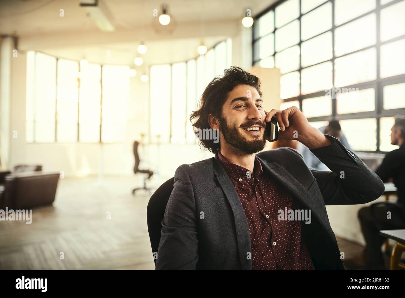 Ein hübscher junger Geschäftsmann, der im Büro mit seinem Handy spricht. Stockfoto