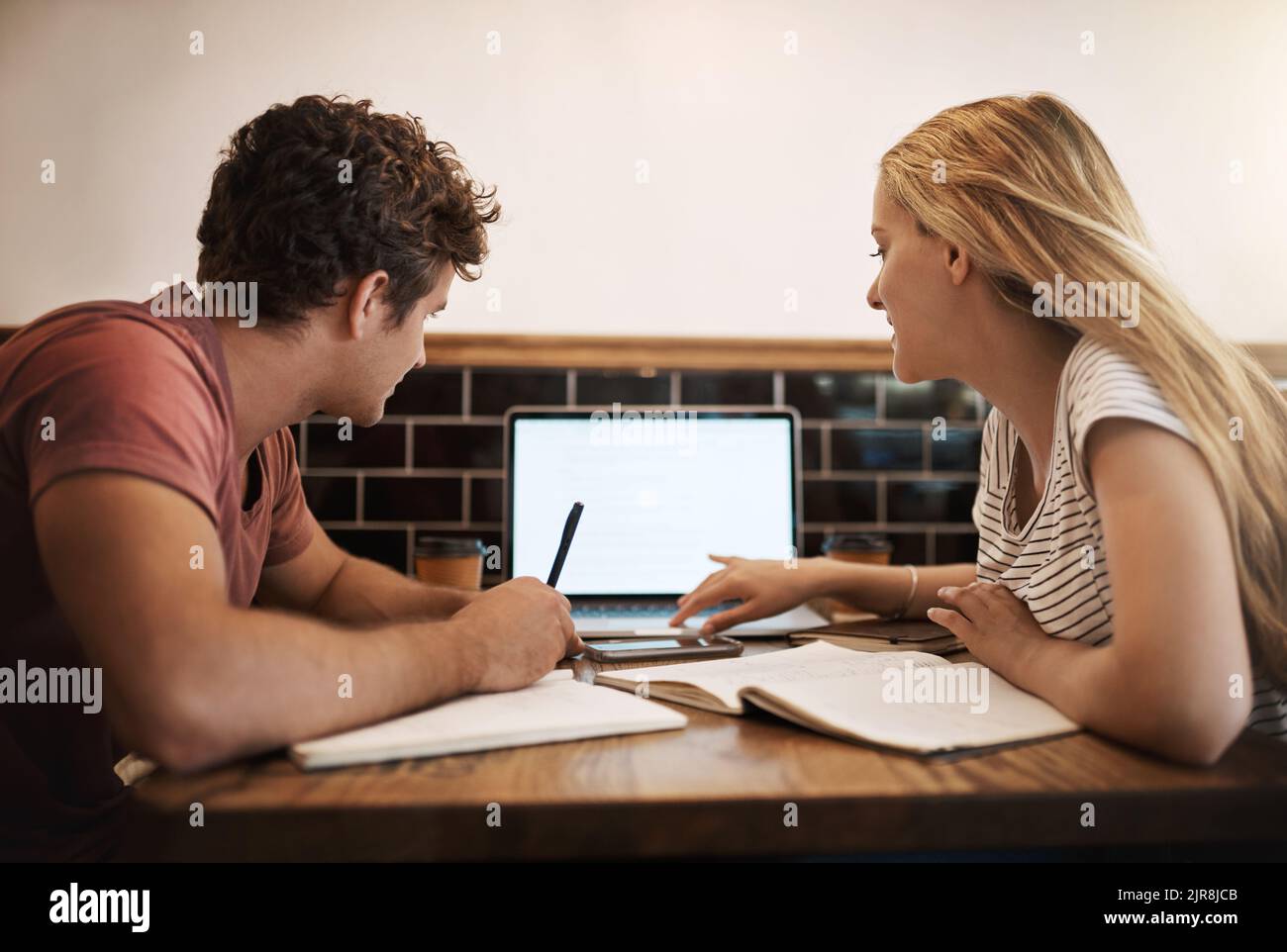 Nutzung von Online-Lernressourcen. Zwei glückliche junge Studenten, die eine Studiensitzung in ihrem Lieblingscafé abhalten. Stockfoto