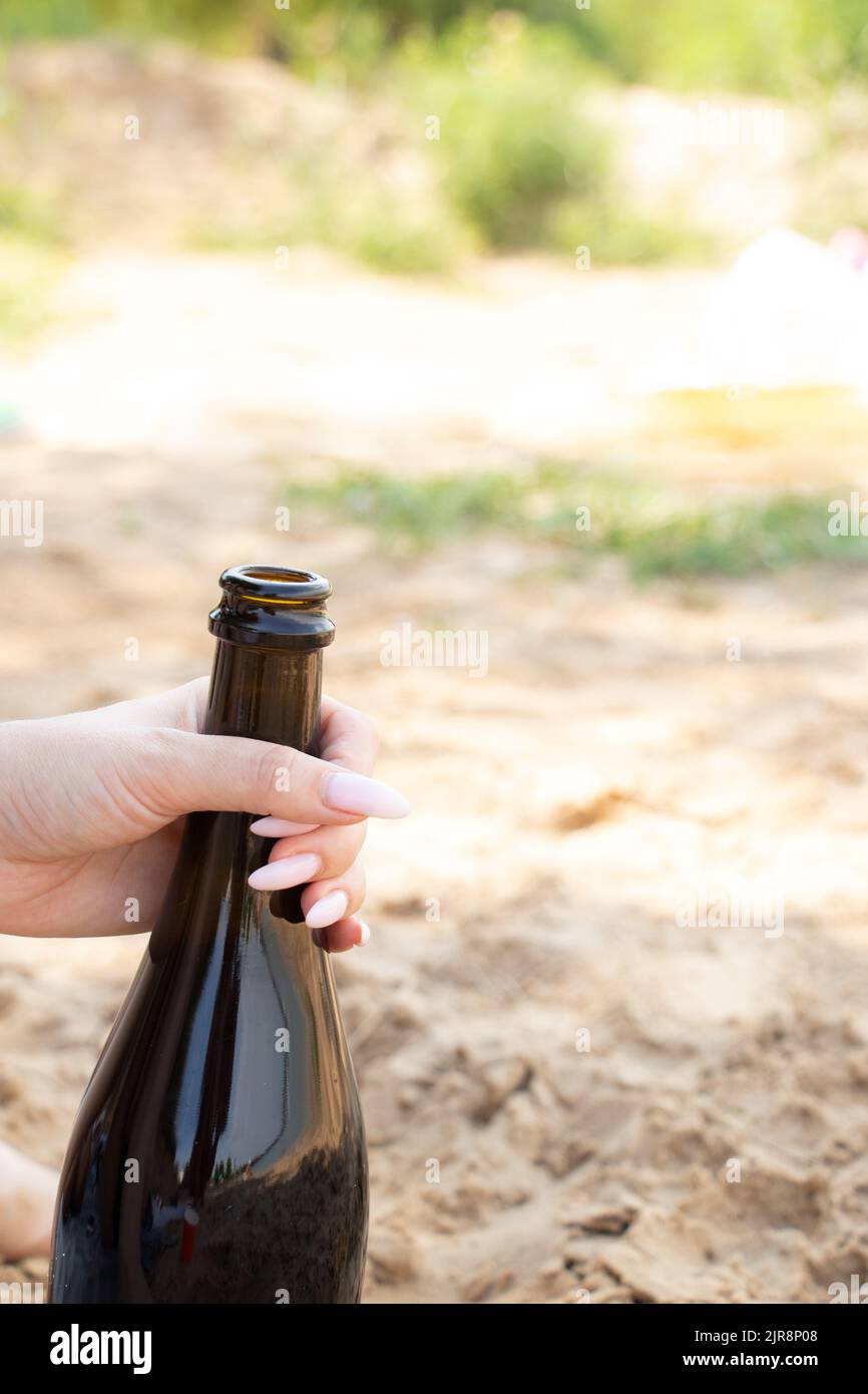 Eine weibliche Hand hält im Sommer am Strand im Urlaub eine Flasche Sekt, eine Flasche Champagner Stockfoto